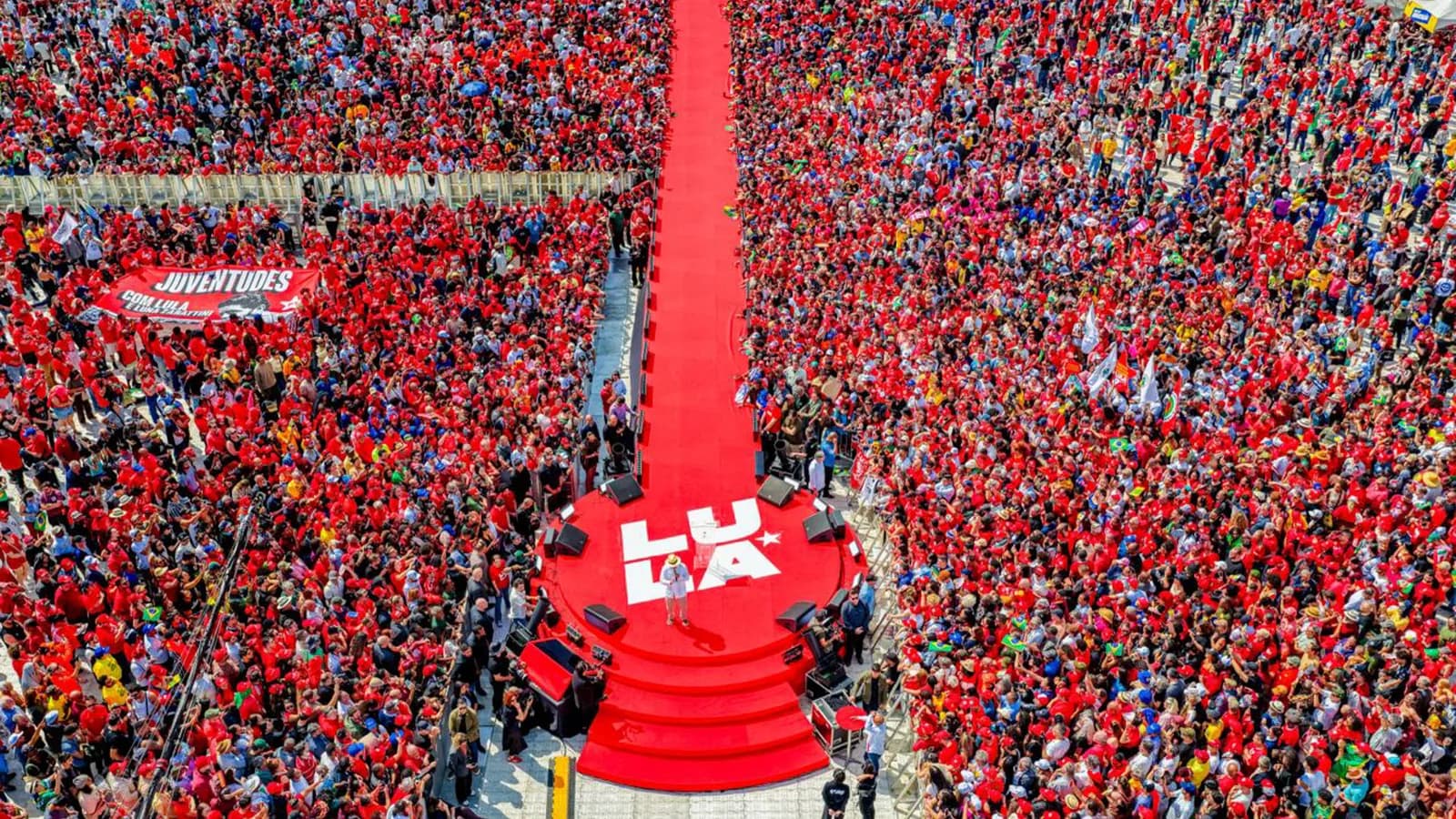 Vista aérea de comício de Lula com multidão vestida de vermelho em torno de um palco com a palavra LULA, durante o lançamento da campanha em agosto de 2026