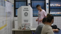 Cabina de votação da Justiça Eleitoral com eleitor se aproximando da urna eletrônica, foto de arquivo