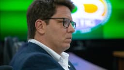 Mario Frias em reunião, de terno, olhando para o lado