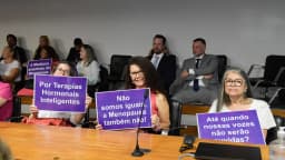 Mulheres participam de audiência pública no Senado sobre menopausa, segurando cartazes de reivindicação