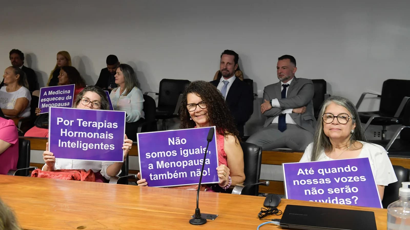 Mulheres participam de audiência pública no Senado sobre menopausa, segurando cartazes de reivindicação