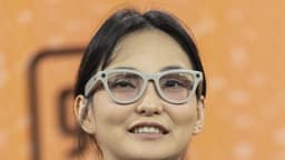 Mulher usa óculos inteligentes Ray-Ban Meta de armação clara, com as lentes das câmeras visíveis nos cantos superiores da armação, durante painel de um evento de tecnologia