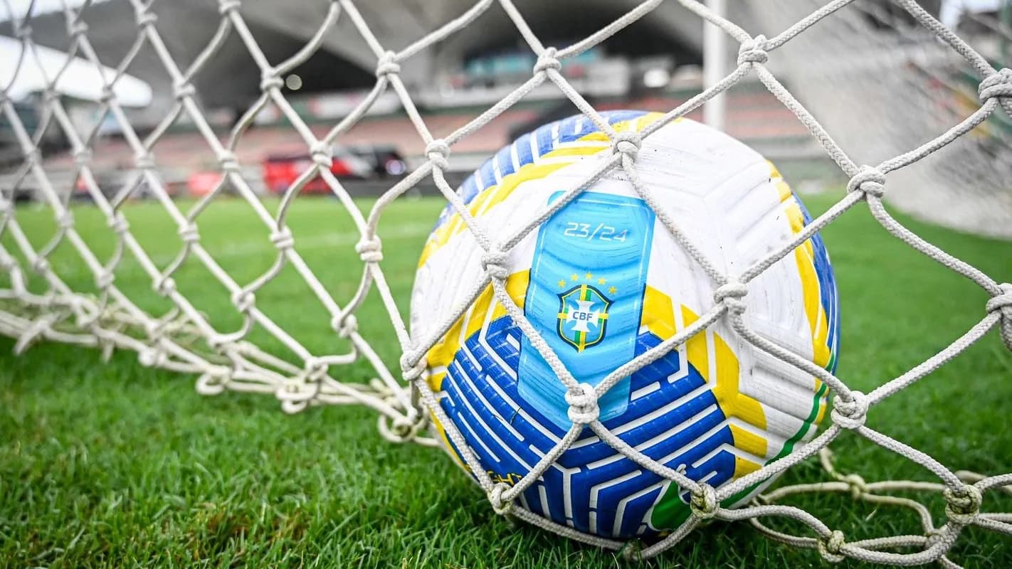 Bola oficial do Brasileirão Feminino presa na rede do gol, em campo de futebol, foto simbólica da competição