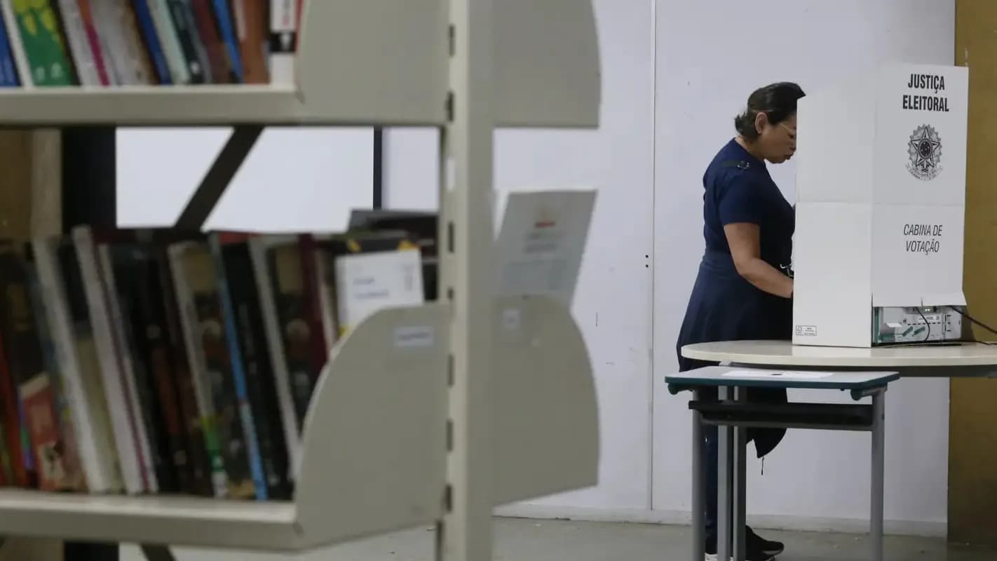 Mulher vota em cabine eleitoral em frente a estante de livros, foto de arquivo da Agência Brasil