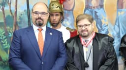 Mateus Simões, de óculos e terno, ao lado de autoridade em evento institucional