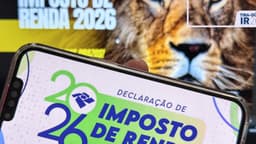 Imagem de arquivo: celular exibe a tela da Declaração de Imposto de Renda 2026, com o logotipo da Receita Federal; ao fundo, peça da campanha do IR 2026 com a imagem de um leão