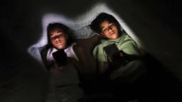 Dois adolescentes deitados no escuro, iluminados pela luz do celular