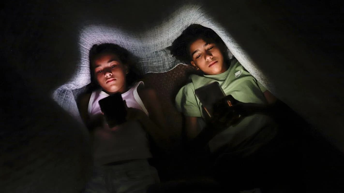 Dois adolescentes deitados no escuro, iluminados pela luz do celular