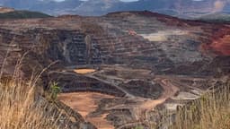 Foto de arquivo de uma cava de mineração a céu aberto, com bancadas e rampas de terra avermelhada, cercada por montanhas em Itabirito, Minas Gerais