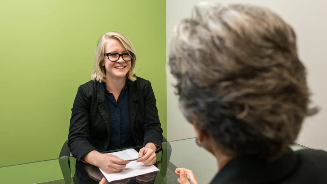Mulher participa de entrevista de emprego sentada à mesa com entrevistadora