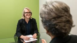 Mulher participa de entrevista de emprego sentada à mesa com entrevistadora