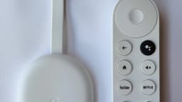 Controle remoto do Google TV ao lado de um Chromecast, com botão de mute visível