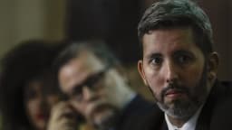 Leandro Grass em primeiro plano, de expressão séria, durante cerimônia no Iphan