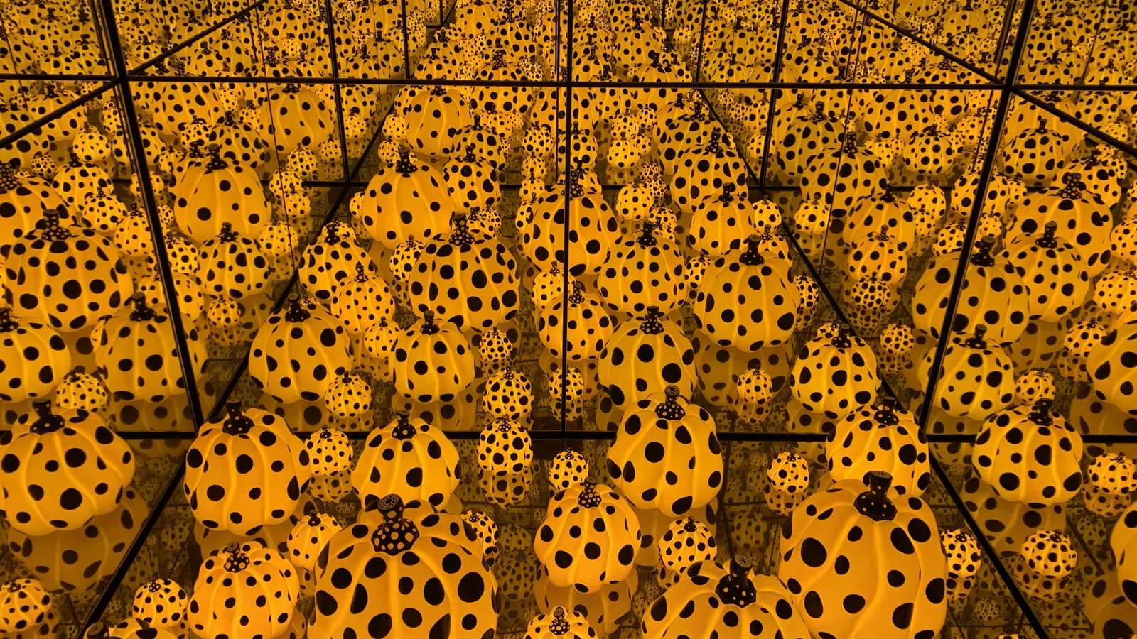 Instalação de abóboras amarelas com bolinhas pretas em sala de espelhos infinitos, obra de Yayoi Kusama