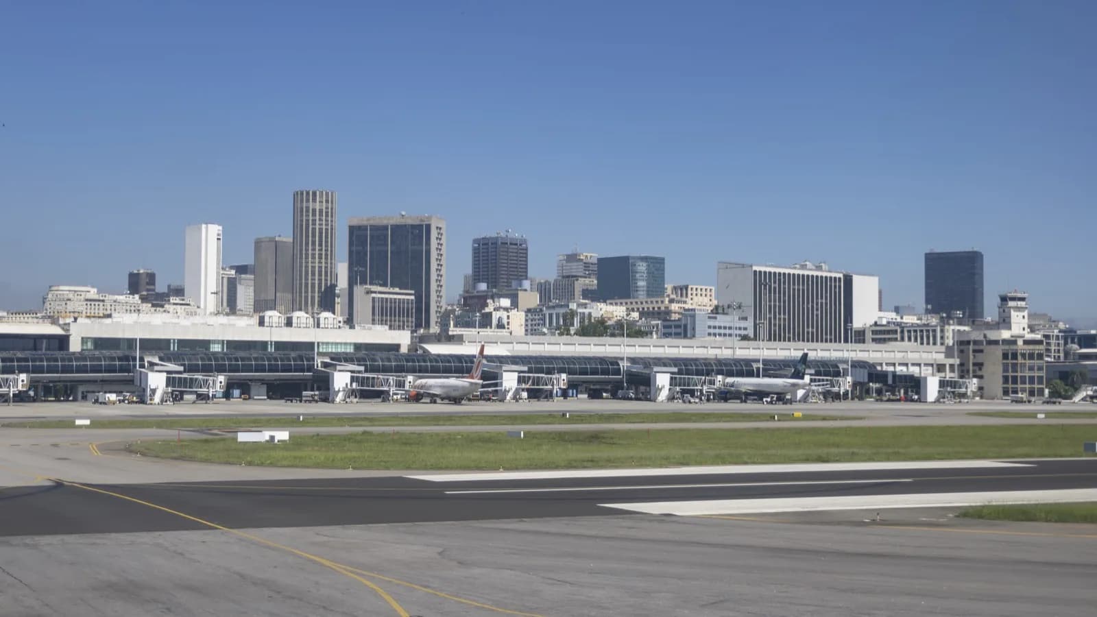 Vista do pátio e da pista do Aeroporto Santos Dumont, no Rio de Janeiro, com aviões estacionados e o centro da cidade ao fundo