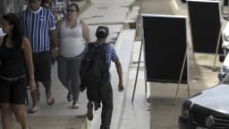 Pedestres caminham por calçada com painéis de propaganda eleitoral