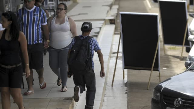 Pedestres caminham por calçada com painéis de propaganda eleitoral
