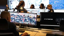 Sala de videomonitoramento com policiais acompanhando câmeras de segurança em telas