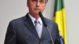Retrato de Jair Bolsonaro em pronunciamento oficial, com bandeira do Brasil ao fundo