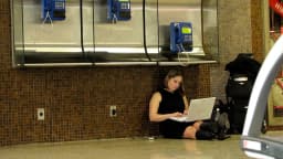 Pessoa sentada no chão usa notebook em espaço público