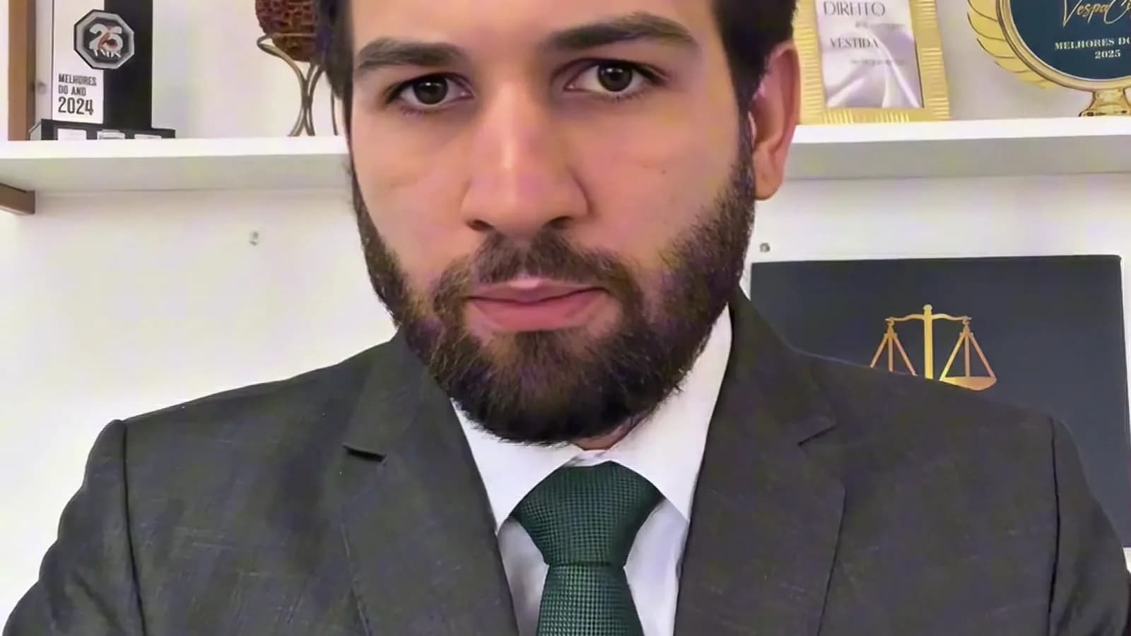 Advogado Pedro Guerra, de terno cinza e gravata verde, fala em frente a uma estante com livros de direito e o símbolo da balança da Justiça, em vídeo sobre regras eleitorais
