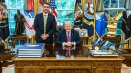 Flávio Bolsonaro em pé ao lado da mesa do presidente dos Estados Unidos, Donald Trump, na Sala Oval da Casa Branca