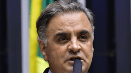 Aécio Neves fala ao microfone durante sessão na Câmara dos Deputados, com a bandeira do Brasil ao fundo