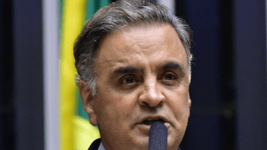 Aécio Neves fala ao microfone durante sessão na Câmara dos Deputados, com a bandeira do Brasil ao fundo