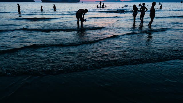 Banhistas na praia de Santos (SP) ao entardecer, com navio ao fundo