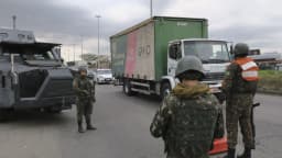 Militares e policiais em operação conjunta contra roubo de cargas no Rio de Janeiro, com blindado e caminhão ao fundo