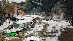 Destroços do avião da Voepass após a queda em Vinhedo (SP), com bombeiro ao fundo cercado por espuma de combate a incêndio