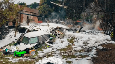 Destroços do avião da Voepass após a queda em Vinhedo (SP), com bombeiro ao fundo cercado por espuma de combate a incêndio