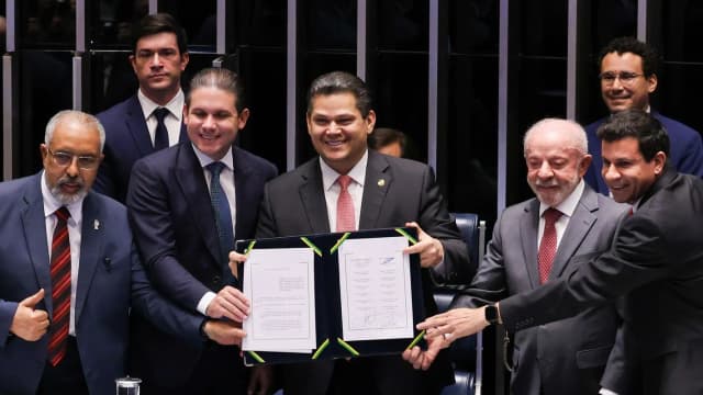 Lula ao lado de Hugo Motta e outras autoridades segurando documento assinado em cerimônia no Congresso