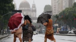 Pessoas caminham sob chuva forte, imagem de contexto sobre mobilização da Defesa Civil para temporais no Sul