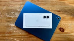Caixa de iPhone com câmera dupla sobre um iPad, em cima de uma mesa de madeira