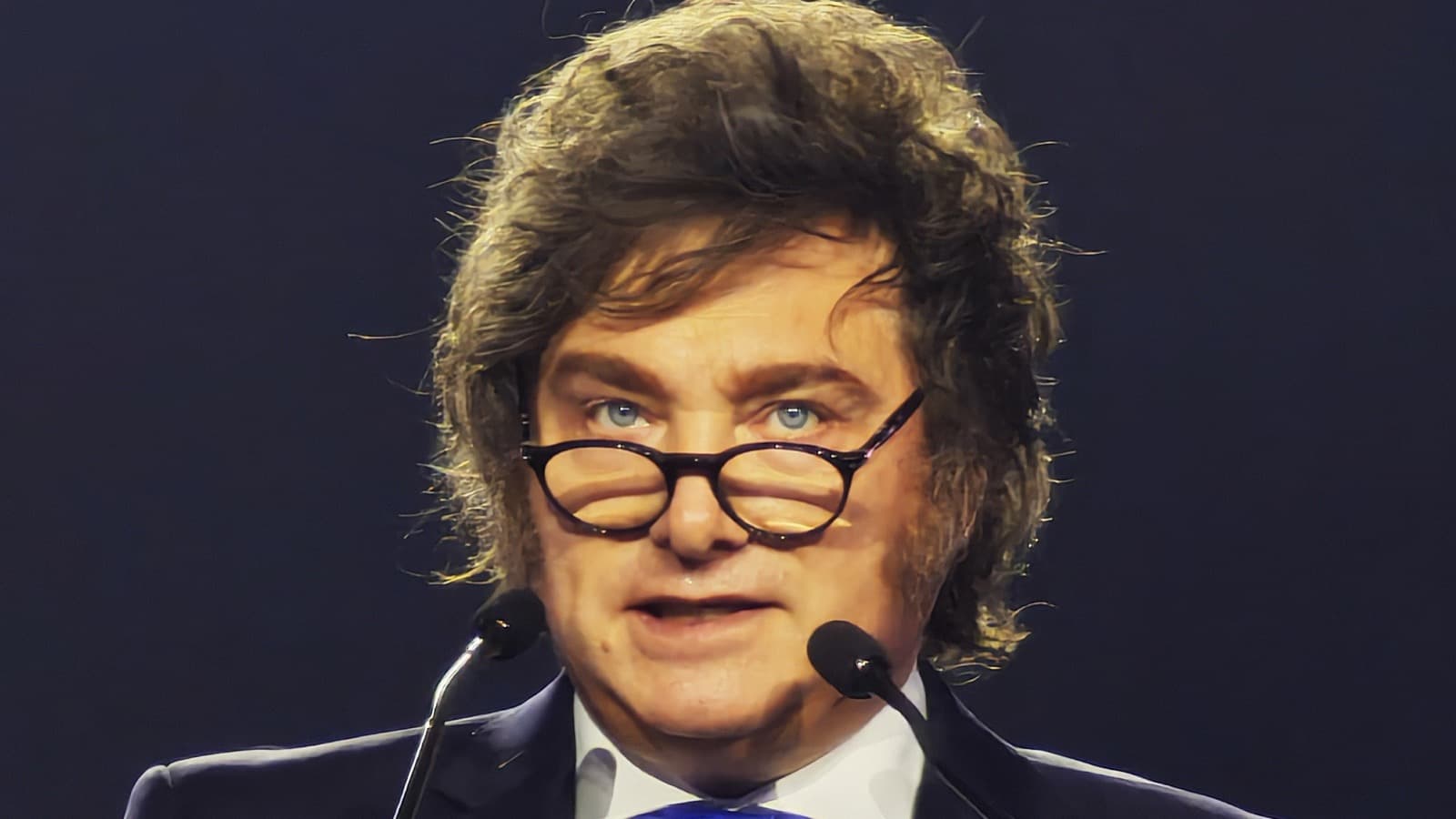 Em foto de arquivo, o presidente da Argentina, Javier Milei, discursa ao microfone, de terno escuro e gravata azul
