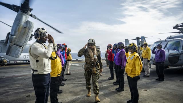 Marinheiros perfilados no convés de um navio de guerra dos EUA fazem continência enquanto um militar caminha entre eles