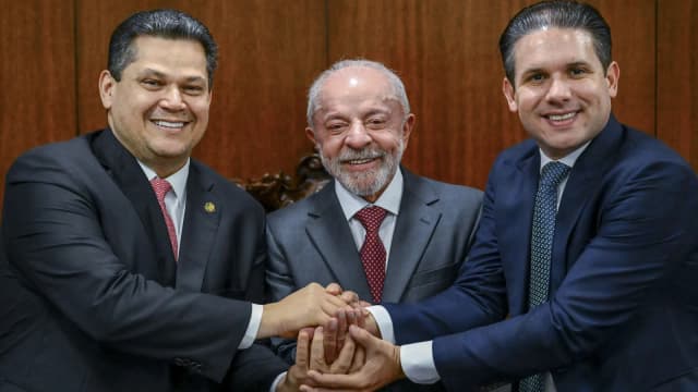 Lula sorri ao cumprimentar dois parlamentares em sessão solene de promulgação de emendas constitucionais na Câmara