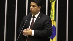 Deputado discursa à tribuna no plenário da Câmara dos Deputados, com bandeira do Brasil ao fundo