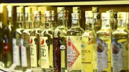 Prateleira com dezenas de garrafas de cachaça de marcas diferentes, com rótulos e selos à mostra; imagem de arquivo