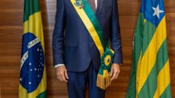Ronaldo Caiado, de terno azul e faixa de governador de Goiás, posa entre a bandeira do Brasil e a de Goiás