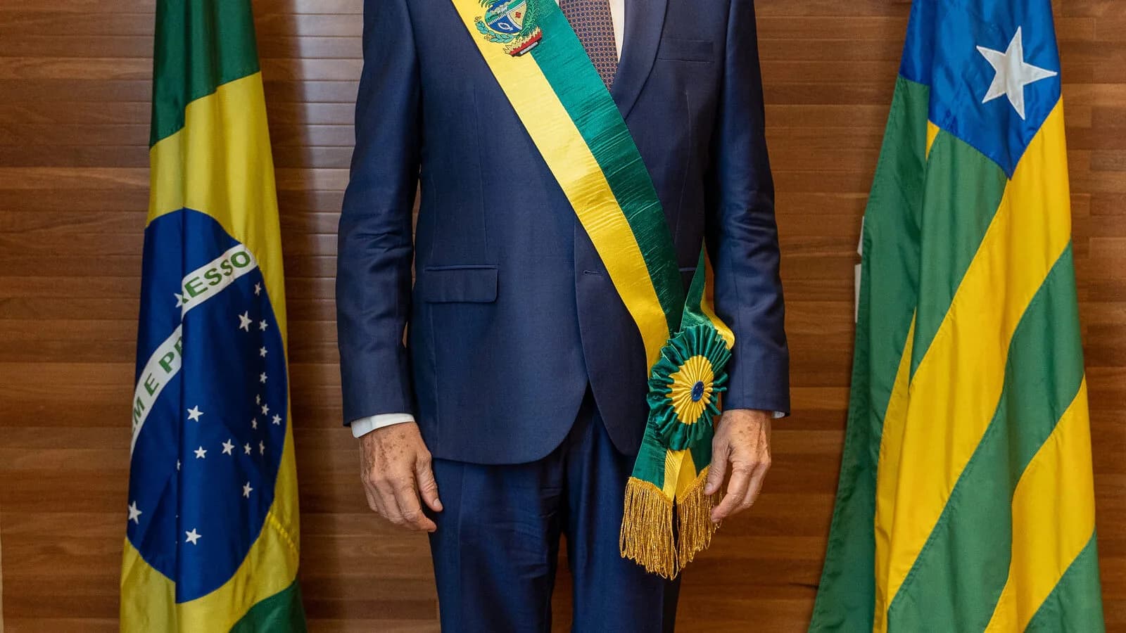 Ronaldo Caiado, de terno azul e faixa de governador de Goiás, posa entre a bandeira do Brasil e a de Goiás