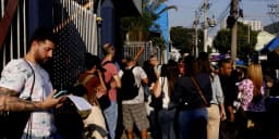 Candidatos em fila para prova de concurso público, checando documentos no celular