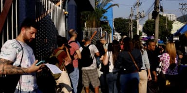 Candidatos em fila para prova de concurso público, checando documentos no celular