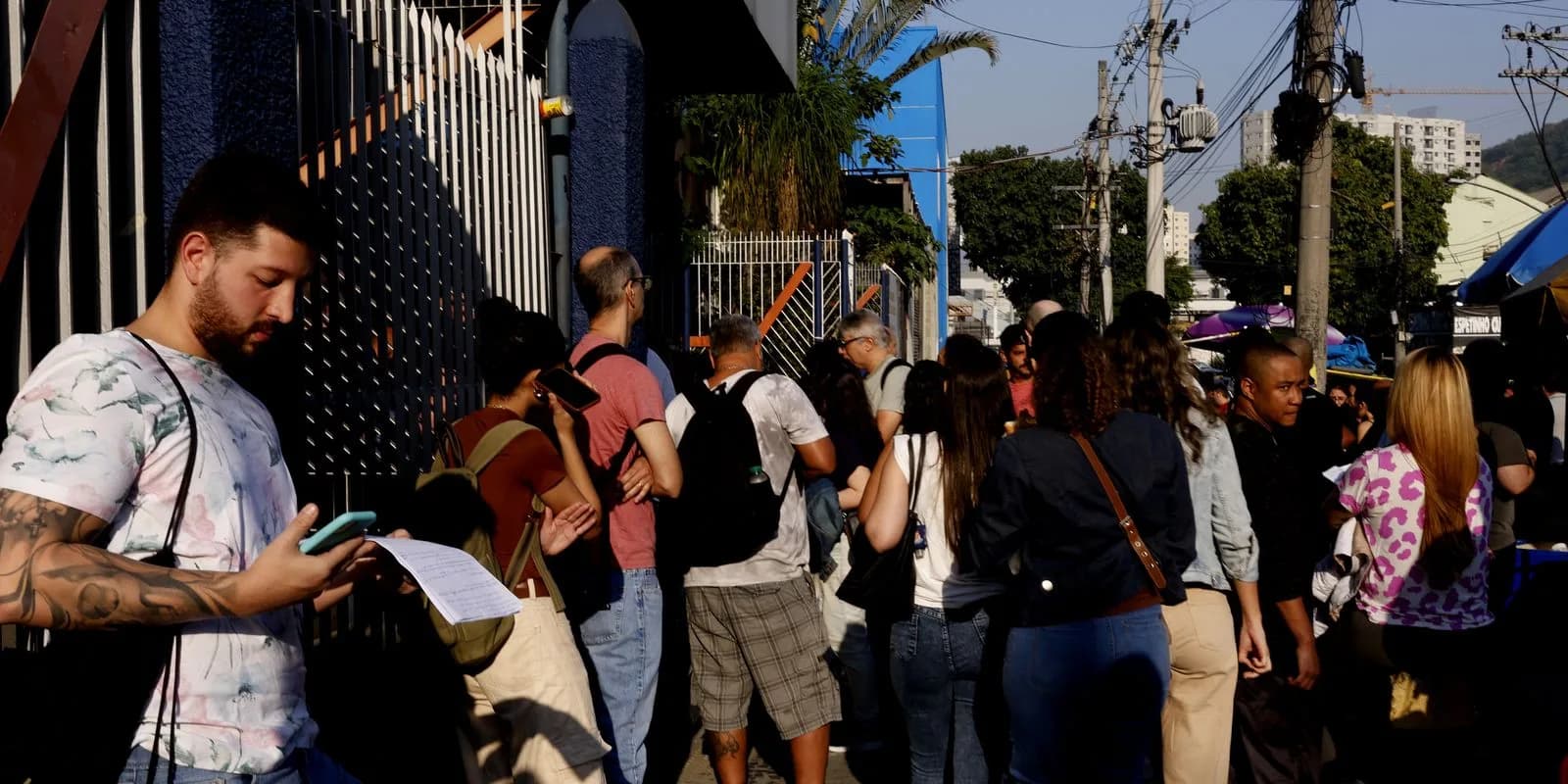 Candidatos em fila para prova de concurso público, checando documentos no celular