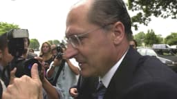 Geraldo Alckmin, de óculos e terno escuro, cercado de fotógrafos durante entrevista