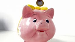 Moeda de um real sendo depositada em um cofrinho em formato de porquinho