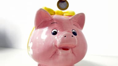 Moeda de um real sendo depositada em um cofrinho em formato de porquinho