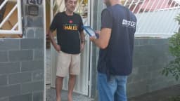 Recenseador do IBGE, identificado por camisa com a logo do instituto, entrevista morador em visita domiciliar