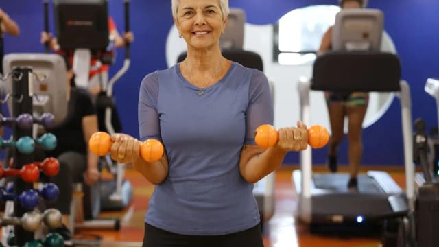 Mulher idosa pratica musculação em academia, atividade associada à saúde do cérebro